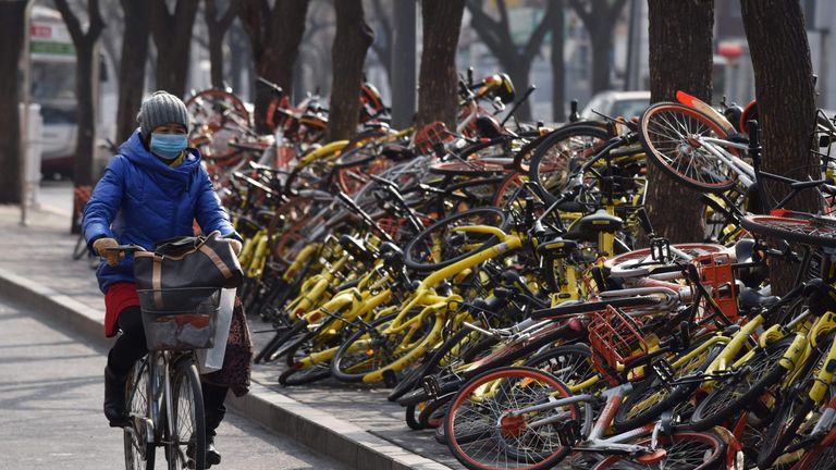 A woman rides past shared bicycles piled beside a road in Beijing on February 21, 2018