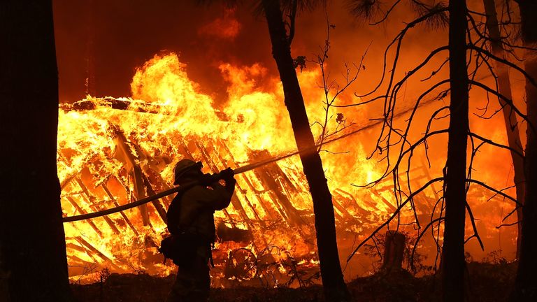A firefighter sprays water on a home next to a burning home as the Camp Fire moves through the area