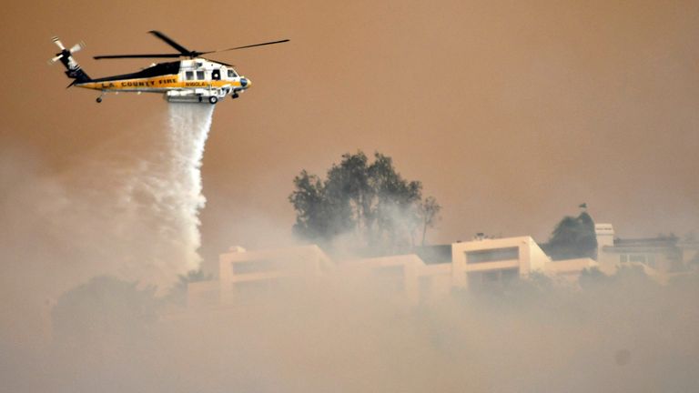 A Los Angeles County Fire Department firehawk makes a water drop through the thick smoke on homes in the hills of Malibu