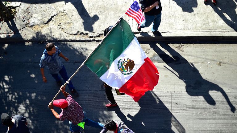 Migrants carry a Mexican and a US flag as they try to get to El Chaparral border crossing