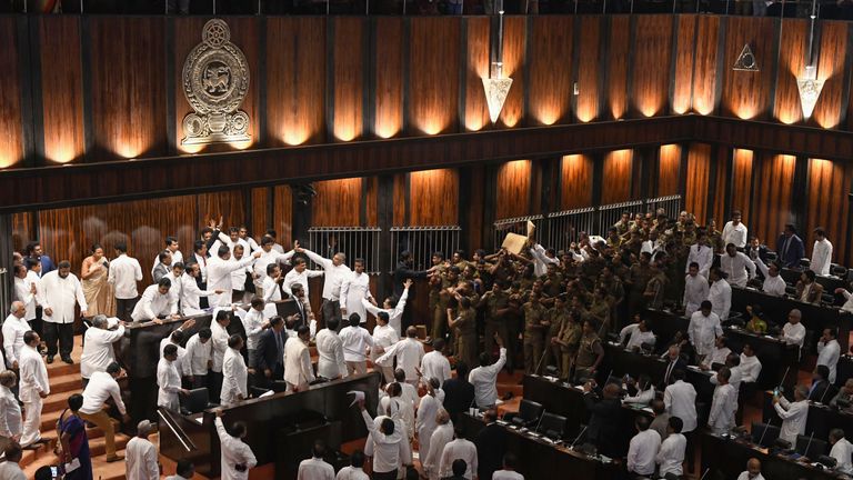 Sri Lankan police (R) gather to escort parliament speaker Karu Jayasuriya in the assembly hall as rival legislators (L) occupy the speaker&#39;s seat in Colombo on November 16, 2018. - Sri Lanka&#39;s parliamentary speaker required police protection as violence returned to the legislature for a second day November 16, with rival factions in the island&#39;s constitutional crisis showing no signs of backing down. A group of legislators occupied speaker Karu Jayasuriya&#39;s chair for 50 minutes and he was only a