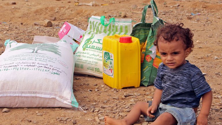 A displaced child from Hodeida sits next to food aid 