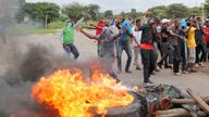 Protesters stand behind a burning barricade during protests on a road leading to Harare