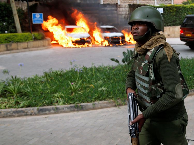 A policeman runs past burning cars at the scene where explosions and gunshots were heard at the Dusit hotel compound, in Nairobi