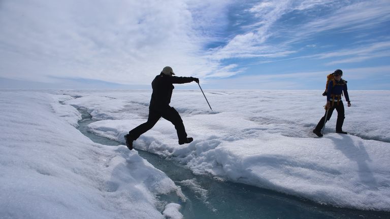 GLACIAL ICE SHEET, GREENLAND - JULY 16: Scientist Ian Joughin of the University of Washington leaps over a small meltwater stream as he walks with Graduate Student, Laura Stevens, from the Massachusetts Institute of Technology and Woods Hole Oceanographic Institution as they conduct research on July 16, 2013 on the Glacial Ice Sheet, Greenland. The scientists set up Global Positioning System sensors to closely monitor the evolution of the surface lakes and the motion of the surrounding ice sheet