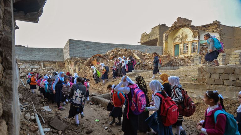 Students walk through a damaged road on their way back from school in Mosul