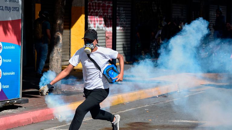 An opposition demonstrator runs with a tear gas canister