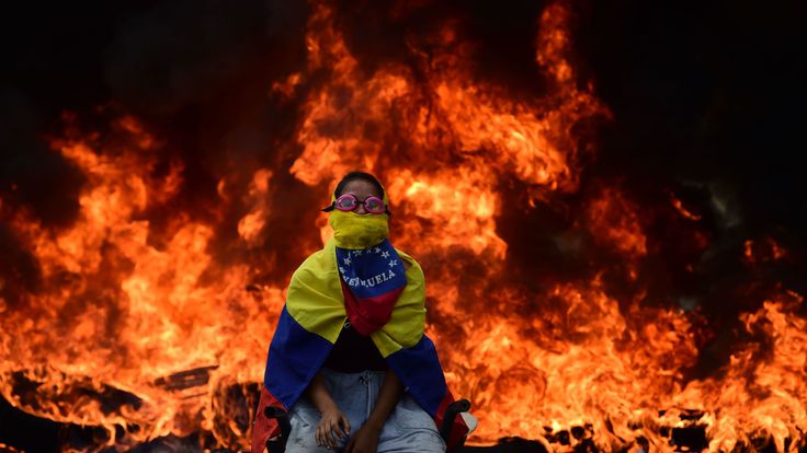 A Venezuelan opposition activist sits in front of a burning barricade 