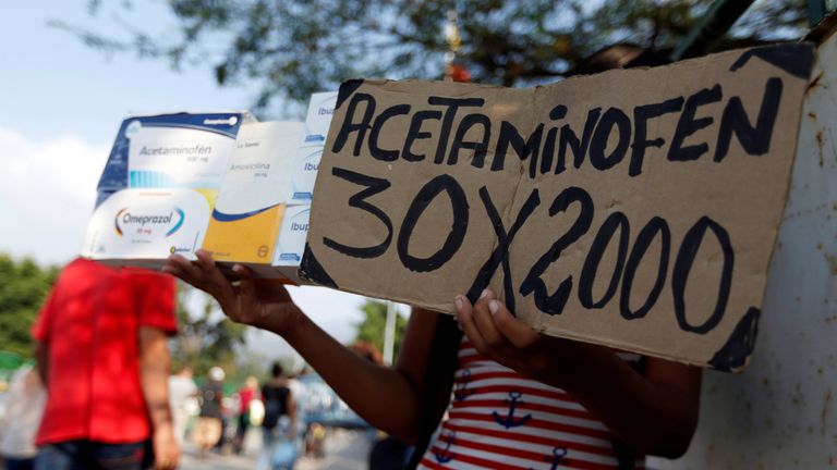A woman holds a sign that reads "Acetaminophen 30 x 2000" over the Simon Bolivar international bridge