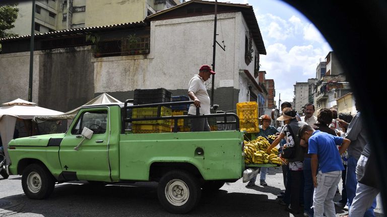 People gather around a man selling bananas in his truck in a street market of Caracas