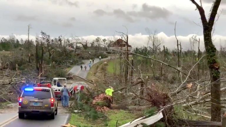 People clear fallen trees and debris on a road following the tornado in Alabama