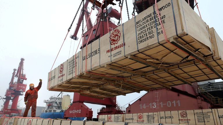 A worker gestures as a crane lifts goods for export onto a cargo vessel at a port in Lianyungang, Jiangsu province