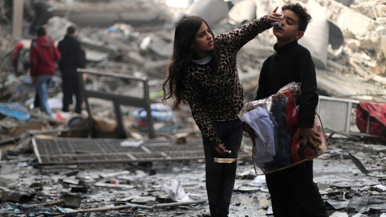 A Palestinian girl cleans the face of her brother outside their destroyed house after an Israeli missile strike
