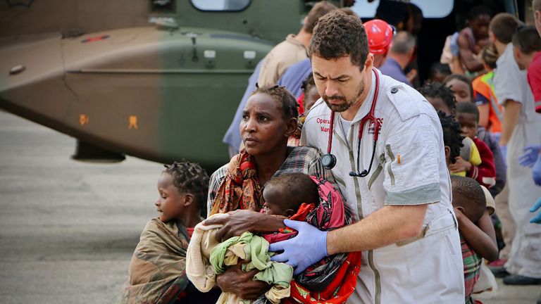 People are escorted to safety by aid workers at the airport of the coastal city of Beira in central Mozambique on March 19, 2019, after the area was hit by the Cyclone Idai. - More than 80 people were rescued by Rescue South Africa and the South African army with helicopters from the Buzi area, province of Safala, where they were stranded since March 15. Rescue workers in Mozambique were racing against time to pluck people off trees and rooftops on March 19, after a monster storm reaped a feared