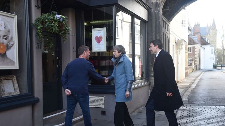 Theresa May talks to a local shopkeeper as she walks through Salisbury with local MP John Glen (right) on the first anniversary of the Skripal poisoning