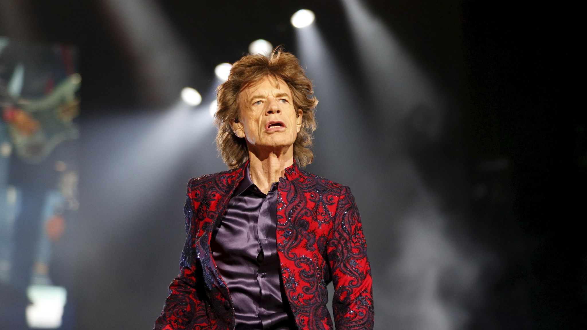 Mick Jagger performing on stage wearing shiny red coat.