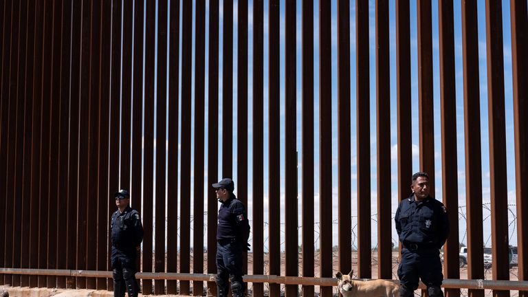 Mexican border police stand at the steel-slate fencing that separates the two countries