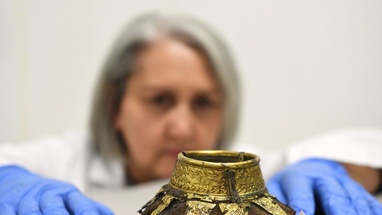 Conservator Claire Reed inspecting the remains of a wooden drinking vessel with a decorated gold neck 