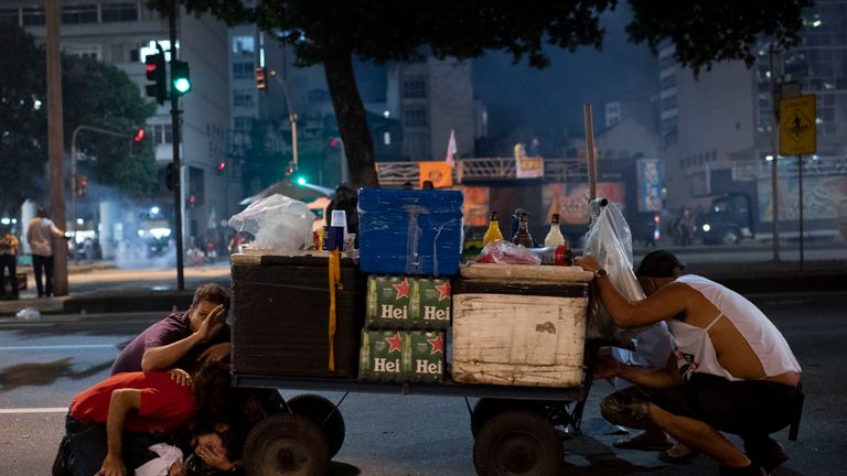 People protect themselves from tear gas and rubber bullets fired by the Brazilian riot police during clashes at the national strike protest
