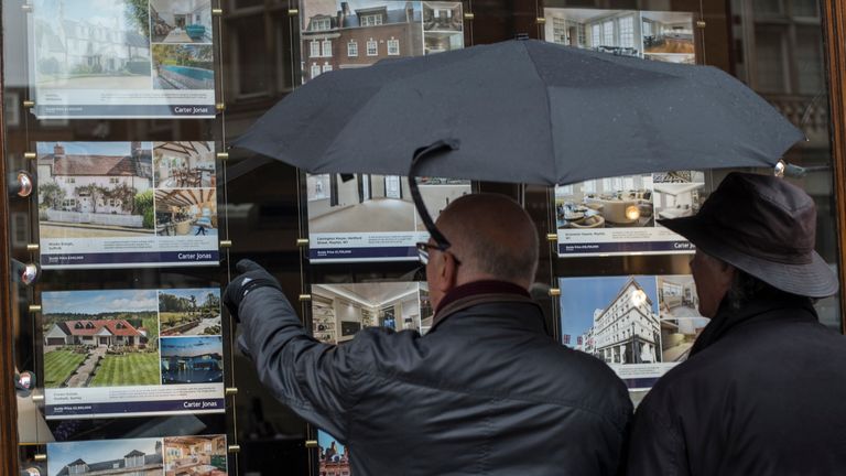 People look at houses for sale in the window of an estate agents