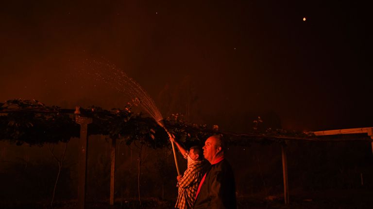 A villager holds a hose as a wildfire comes close to his house at Amendoa in Macao, central Portugal on July 21, 2019. - More than a thousand firefighters battled to control wildfires in central Portugal that have forced village evacuations, in a region where dozens were killed in huge blazes in 2017. The firefighters were deployed to tackle three fires in the mountainous and heavily forested Castelo Branco region, 200 kilometres north of Lisbon, according to the website of the Civil Protection. (Photo by PATRICIA DE MELO MOREIRA / AFP)        (Photo credit should read PATRICIA DE MELO MOREIRA/AFP/Getty Images)