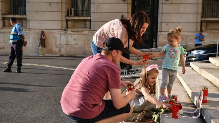 A family lights candles in Bucharest next to a portrait of Alexandra