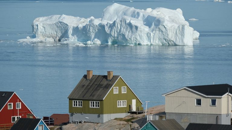 ILULISSAT, GREENLAND - JULY 30: An iceberg floats in Disko Bay behind houses during unseasonably warm weather on July 30, 2019 in Ilulissat, Greenland. The Sahara heat wave that recently sent temperatures to record levels in parts of Europe is arriving in Greenland. Climate change is having a profound effect in Greenland, where over the last several decades summers have become longer and the rate that glaciers and the Greenland ice cap are retreating has accelerated.   (Photo by Sean Gallup/Getty Images)