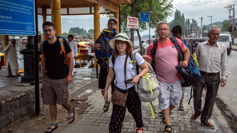 Tourists carry their luggage as they walk on the banks of Dal Lake before leaving Srinagar 