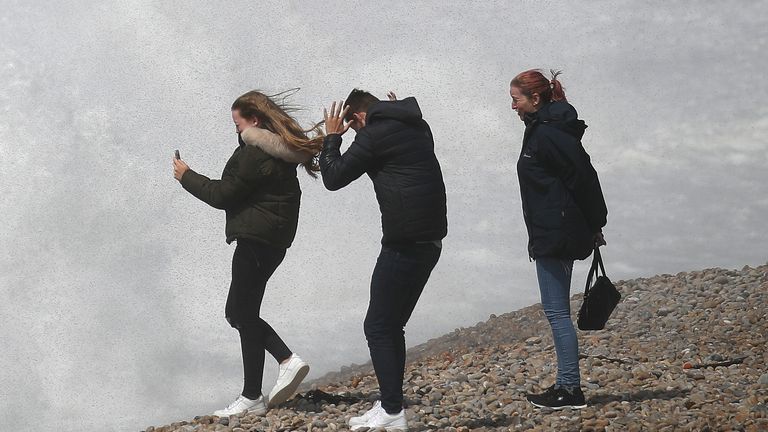 People look out to sea as waves crash against Chesil beach in Dorset