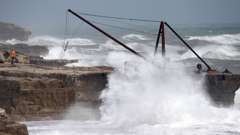 A person looks out as waves crash against rocks at Portland Bill in Dorset