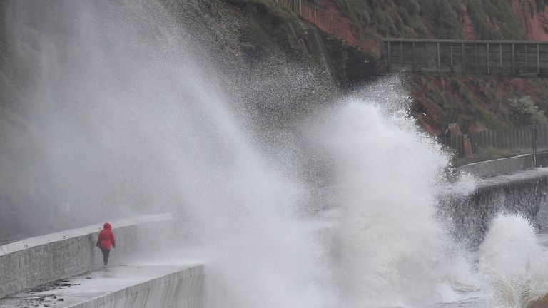 A woman shields herself from large waves and high winds at Dawlish