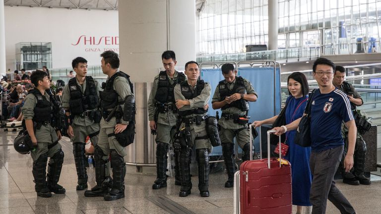 Passengers walk past police guarding the entrance to Hong Kong International Airport