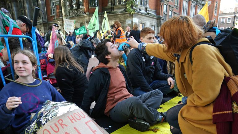 A protester, who has glued himself to the ground at Millbank near to the junction with Great College Street, receives refreshment during an Extinction Rebellion (XR) protest in Westminster, London.