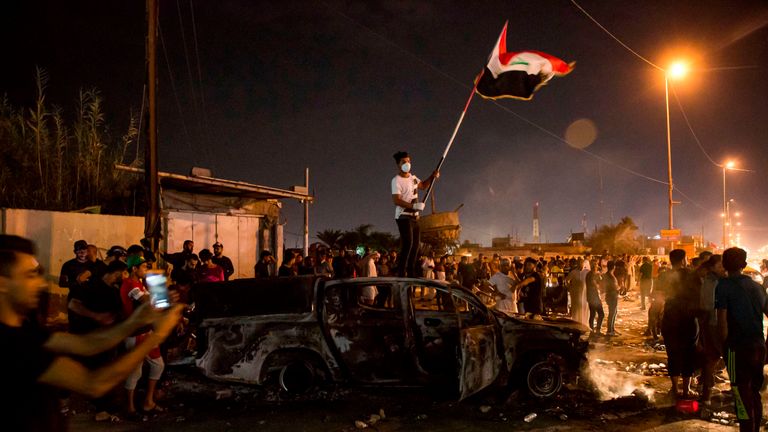 A protester waves a national flag as he stands on a burnt-out police vehicle in Basra