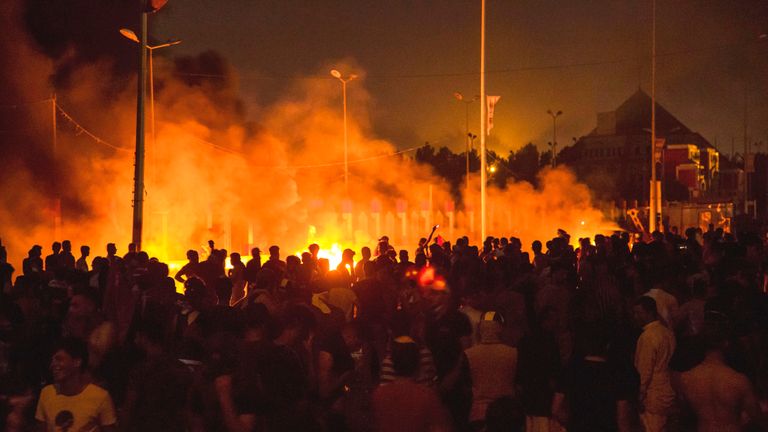 Protesters walk past fires in the street outside the local government headquarters in Basra