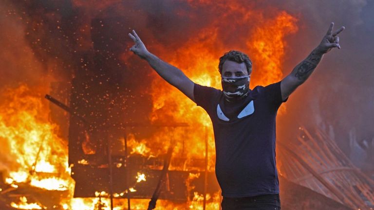A protester flashes the V for victory sign as a riot police vehicle burns in Baghdad on Thursday