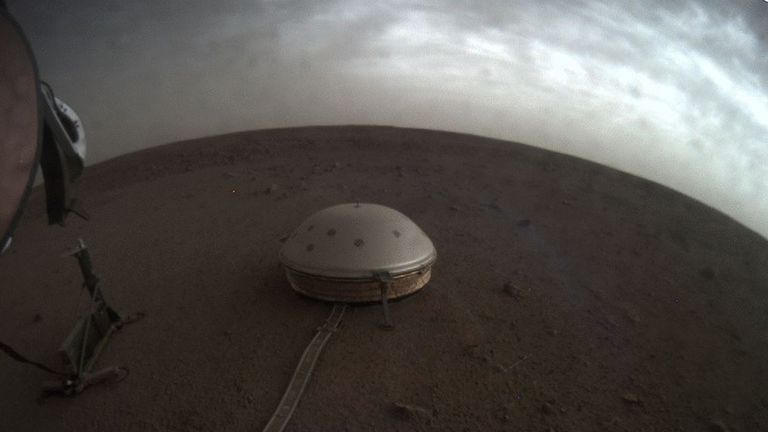 Norii plutesc deasupra unui seismometru acoperit de cupolă, cunoscut sub numele de SEIS, al navei spațiale Insight a NASA, pe suprafața lui Marte.  Imagine: NASA / JPL-Caltech