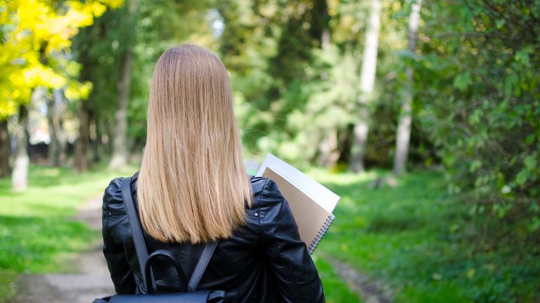 Rear view of teen girl outdoor in the park going back to school
