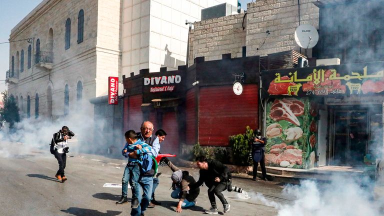A Palestinian journalist carries away a child as other photojournalists assist a falling woman as they walk amidst tear gas canisters
