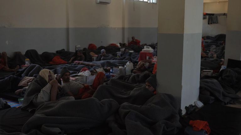 Dozens of prisoners are couped up in a large room, while others are in groups in cells