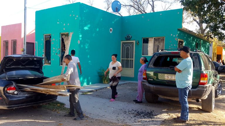 Residents stand in front of a home riddled with bullet holes after a gun battle