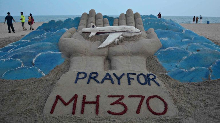 Beachgoers walk past a sand sculpture with a message of prayers for missing flight MH370