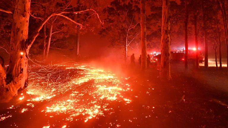 Burning embers cover the ground as firefighters (back R) battle against bushfires around the town of Nowra in the Australian state of New South Wales on December 31, 2019