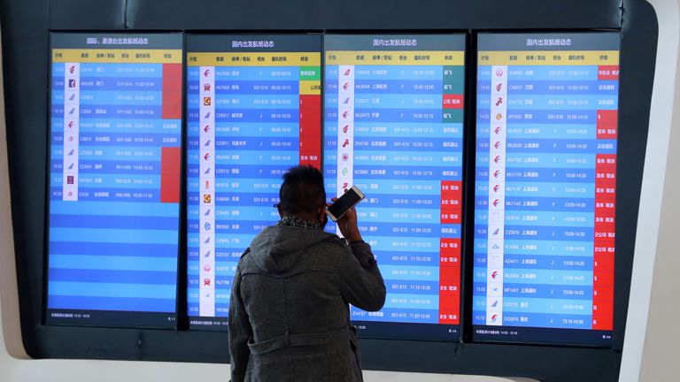 A man stands in front of a screen showing that multiple departure flights have been cancelled at an airport in Wuhan, Hubei province