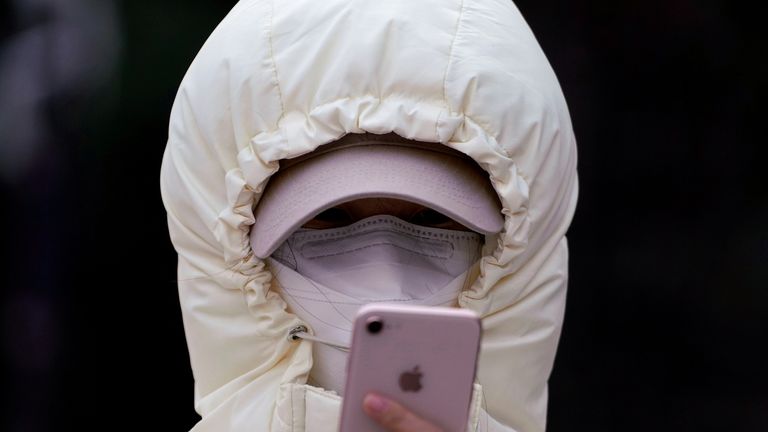 A woman wearing a mask and her hood pulled tight checks her phone in Shanghai