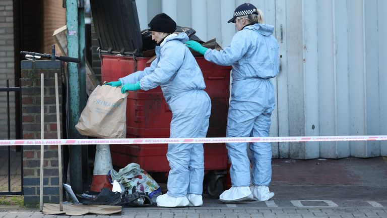 Scenes of crime officers (SOCO) search through a bin near the scene