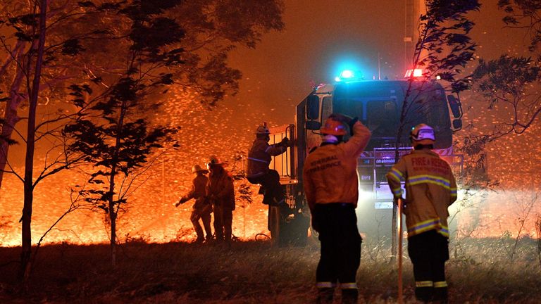 Firefighters hose down trees as they battle against bushfires around the town of Nowra in the Australian state of New South Wales on December 31, 2019