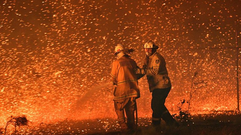 This picture taken on December 31, 2019 shows firefighters struggling against the strong wind in an effort to secure nearby houses from bushfires near the town of Nowra in the Australian state of New South Wales