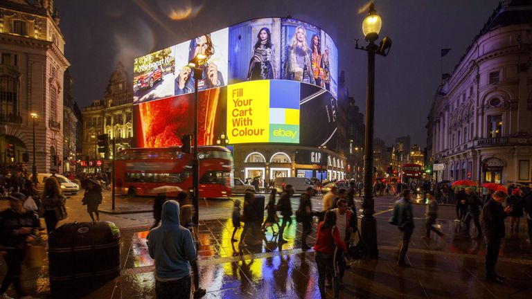 Pedestrians walk past the Piccadilly Circus advertisement screens in London on October 26, 2017 after they were switched back on after a major refurbishment. The world-famous Piccadilly Circus advertising boards were switched back on on October 26, 2017 after being switched off in January for a major refurbishment. Landsec, the owner of Piccadilly Lights, has replaced the original patchwork of screens with a single state-of-the-art 4K LED digital screen and live technology hub, which allows the 