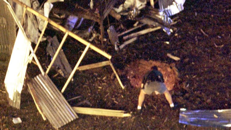 A law enforcement officer peers into the crater caused by a bomb blast in Atlanta's Centennial Olympic Park early July 27, tearing apart an audio tower at rear and killing at least two people and injuring dozens